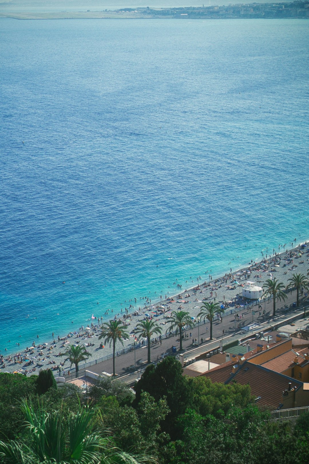 People sunbathing and swimming on a pebble beach next to the ocean.